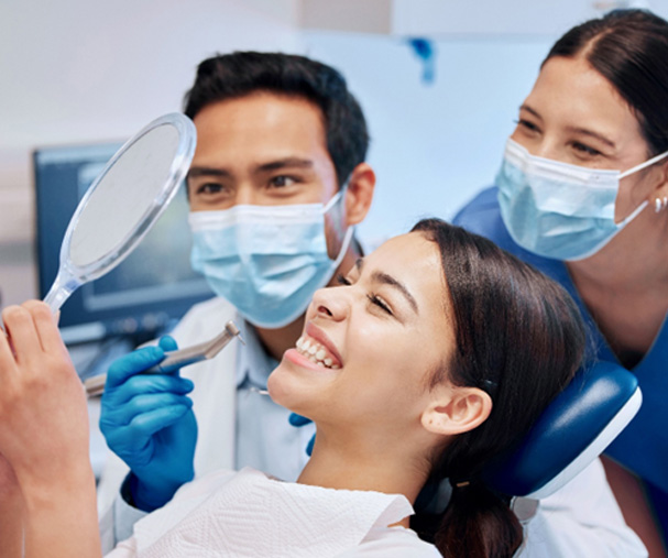 Patient smiling at reflection with dentist and dental hygienist