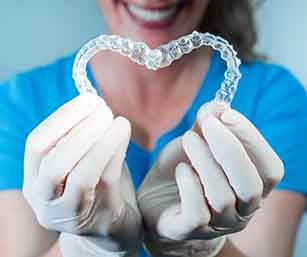 Dentist in blue scrubs and white gloves holding Invisalign in a heart shape