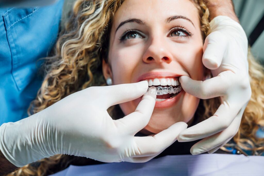 A dentist helping a woman put on her Invisalign aligners