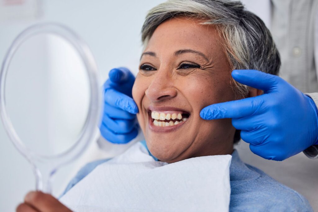 A woman looking at her smile in the mirror at the dentist’s office