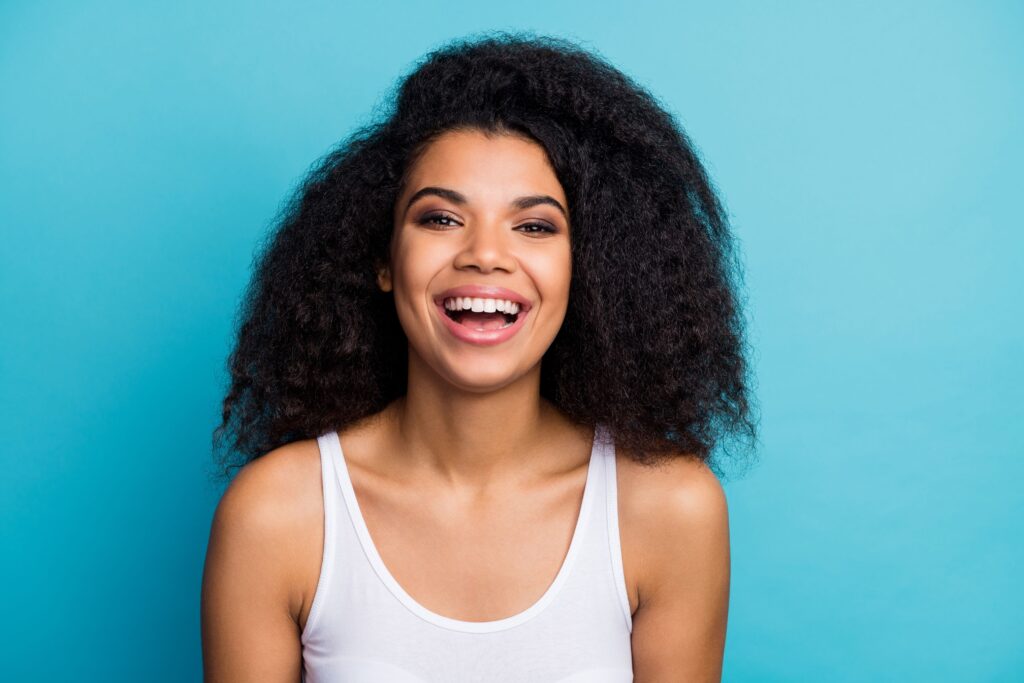 Woman with dark hair in white tank top smiling with light blue background